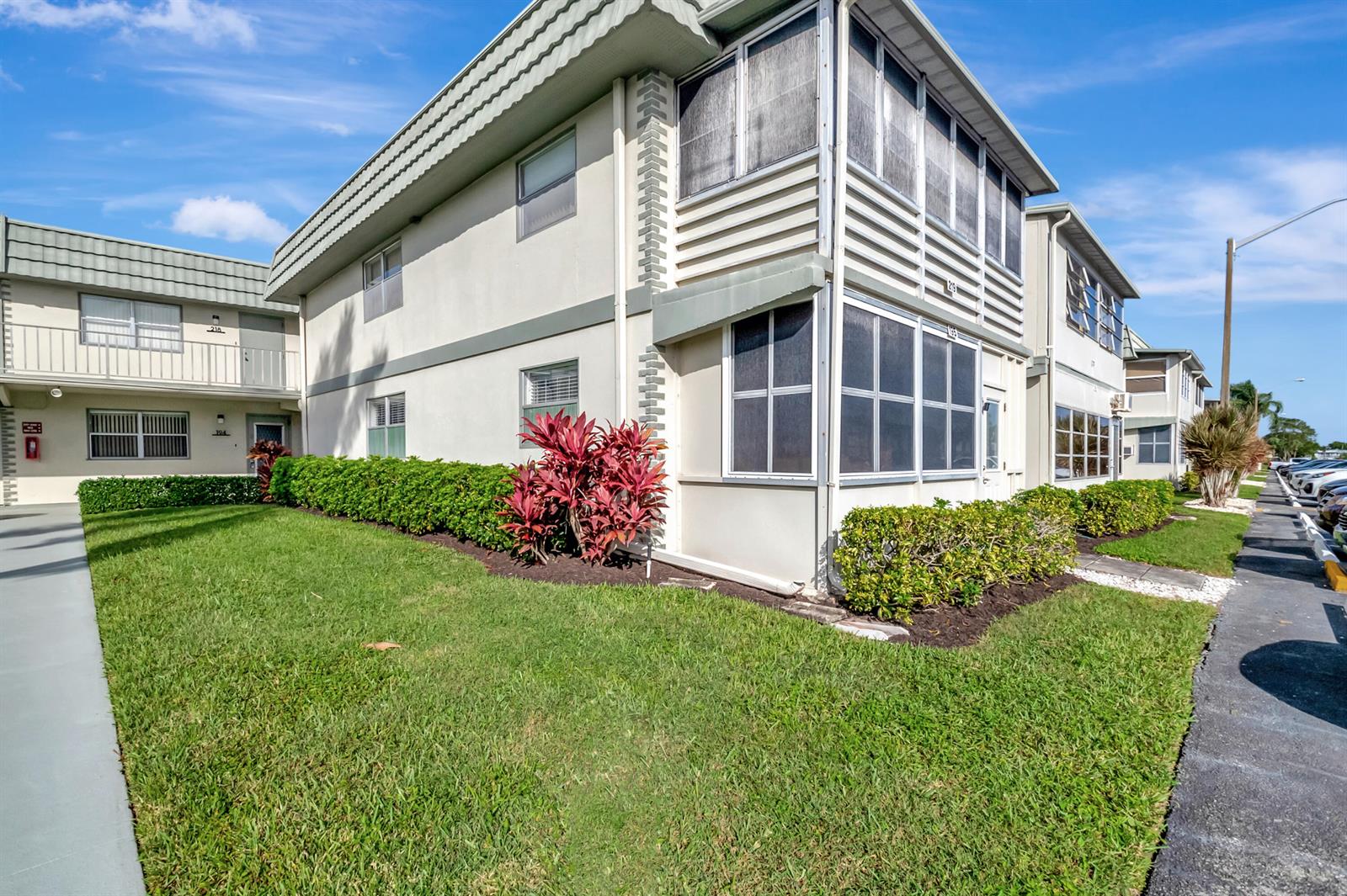 A two-story apartment building features a screened-in porch, landscaped hedges, and a grassy lawn — 195 Monaco E # 195, Delray Beach FL 33446, DELRAY BEACH, FL