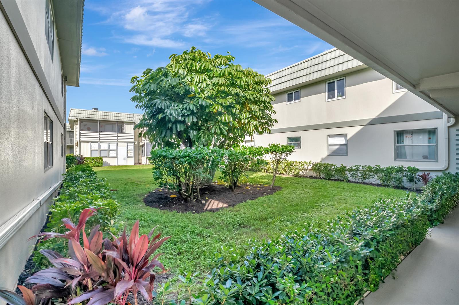A courtyard with a central tree and shrubs sits between two multi-story apartment buildings — 195 Monaco E # 195, Delray Beach FL 33446, DELRAY BEACH, FL