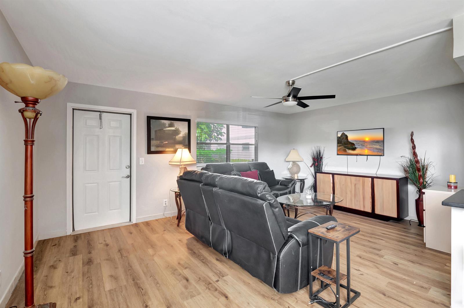 A living room features wood-look flooring, a black leather sofa, and a wall-mounted television — 195 Monaco E # 195, Delray Beach FL 33446, DELRAY BEACH, FL