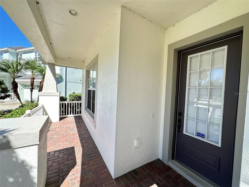 A covered front porch features brick pavers, a dark door with glass panes, and stucco walls — 8120 TURKEY HILL COURT, TAMPA, FL