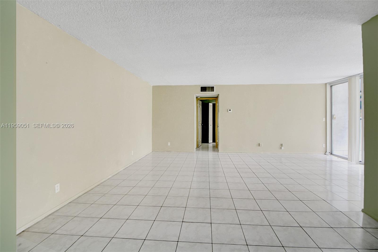 An empty room features white tiled flooring, beige walls, and a sliding glass door — 942 NE 199th St # 2F, Miami FL 33179, MIAMI, FL