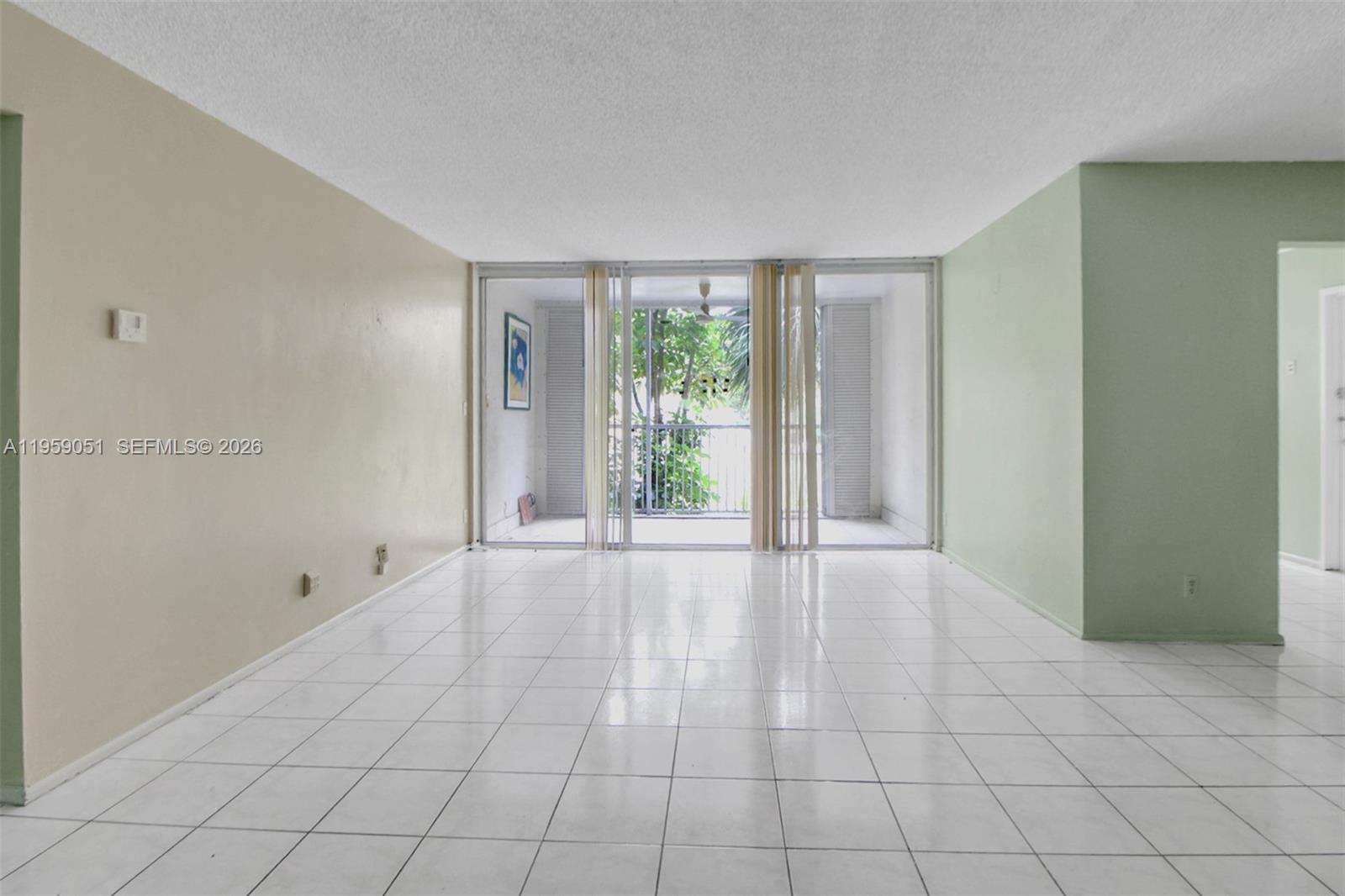 An empty living room features white tile flooring, light-colored walls, and a sliding glass door — 942 NE 199th St # 2F, Miami FL 33179, MIAMI, FL
