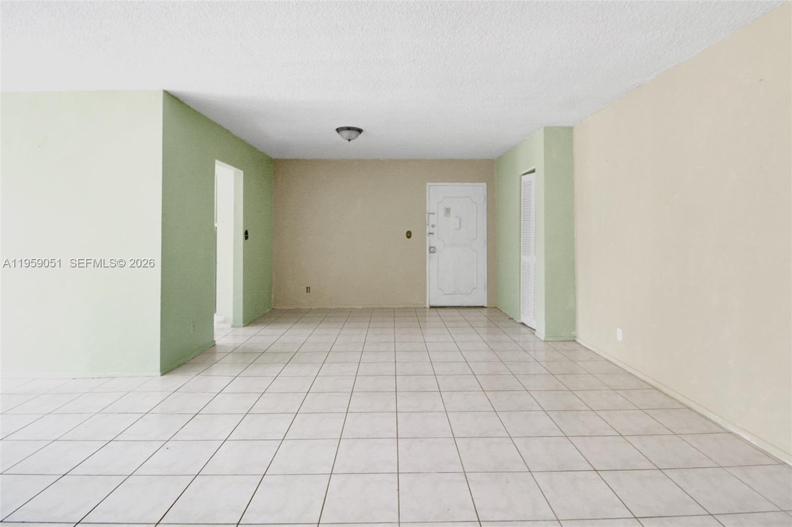 An empty room features light-colored tile flooring, beige and green walls, and a white door — 942 NE 199th St # 2F, Miami FL 33179, MIAMI, FL