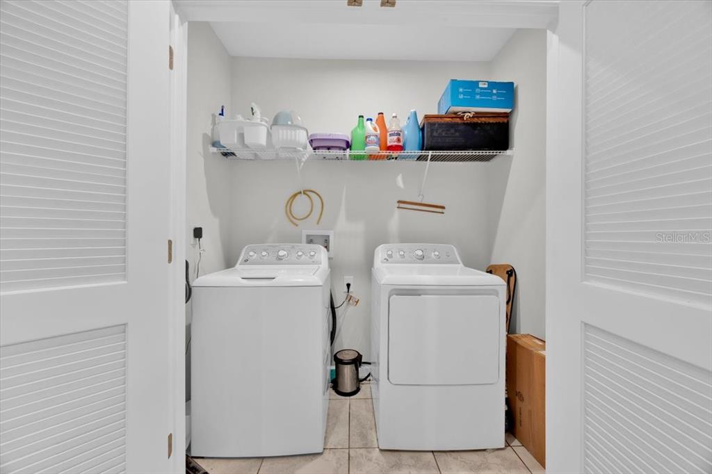 A laundry closet contains a white washer and dryer beneath a wire storage shelf — 145 PIAVE STREET, HAINES CITY, FL