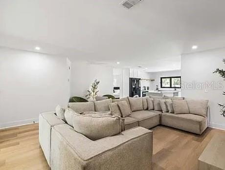 A spacious living room features a large beige sectional sofa on light wood flooring — 5910 DENVER STREET NE, ST PETERSBURG, FL