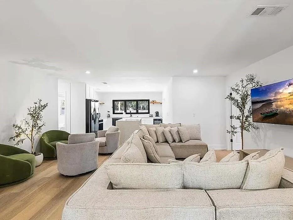 A bright open-concept living room features a large sectional sofa, swivel chairs, and a kitchen — 5910 DENVER STREET NE, ST PETERSBURG, FL