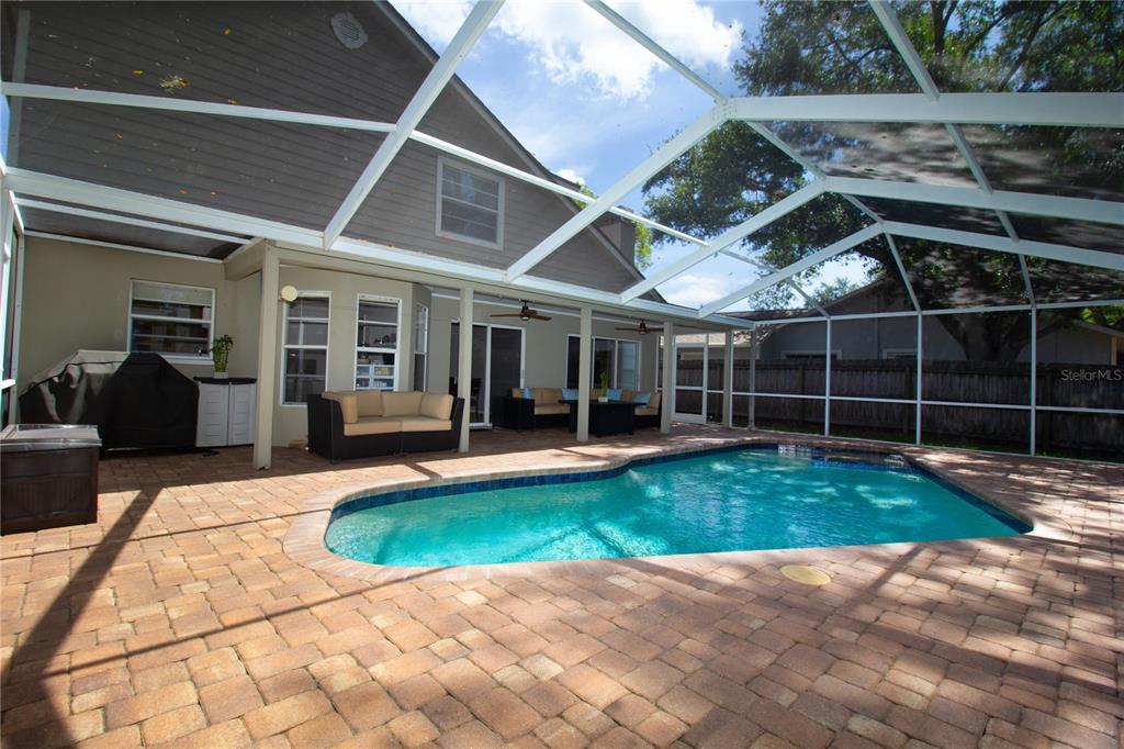 A screened-in patio features a swimming pool and brick pavers next to a house — 1564 COLONY COURT, PALM HARBOR, FL