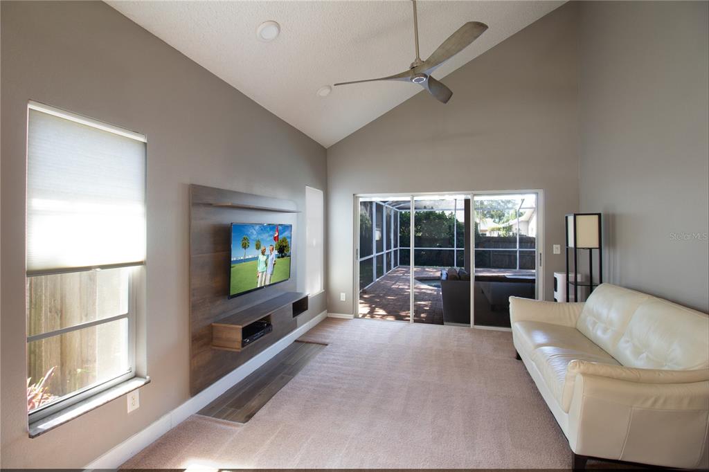 A living room features a vaulted ceiling, a wall-mounted television, and sliding doors to a patio — 1564 COLONY COURT, PALM HARBOR, FL