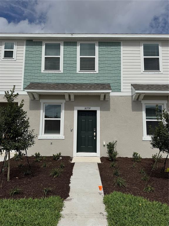A two-story townhouse exterior features a dark green front door and light green shingle siding — 16559 SAN NICOLA PLACE, BRADENTON, FL