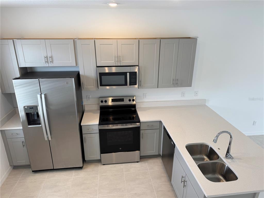 A modern kitchen features light gray cabinets, stainless steel appliances, and light-colored countertops — 16559 SAN NICOLA PLACE, BRADENTON, FL