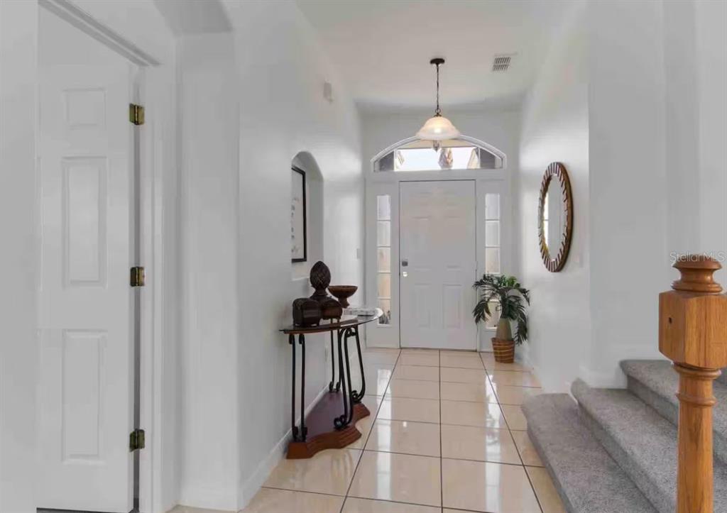 A bright entryway features tiled flooring, a wooden staircase, and a white front door — 943 CORVINA DRIVE, DAVENPORT, FL