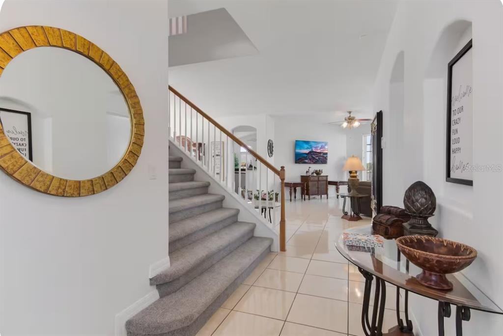A bright entryway features a carpeted staircase, tile flooring, and a round gold-framed wall mirror — 943 CORVINA DRIVE, DAVENPORT, FL