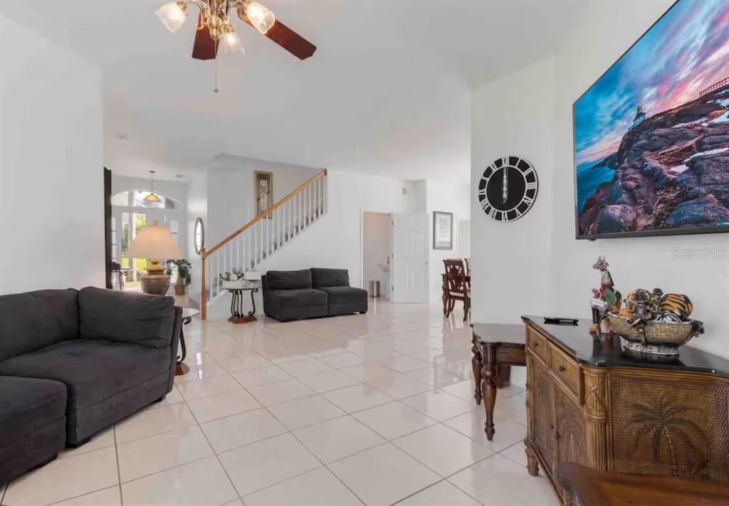 A spacious living room features light tile flooring, a staircase, and a wall-mounted television — 943 CORVINA DRIVE, DAVENPORT, FL