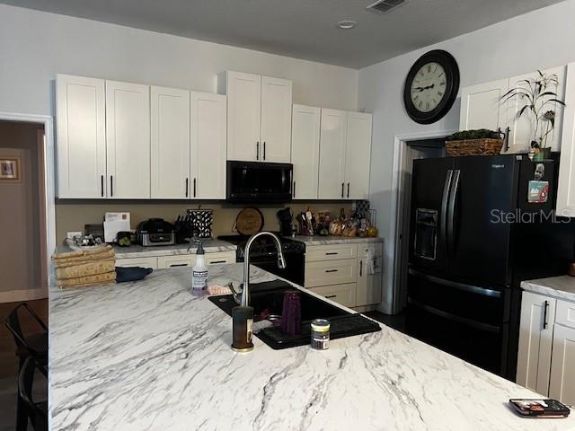 A kitchen features white cabinets, a marble-patterned island countertop, and a black refrigerator — 1 GRAYTWIG COURT W, HOMOSASSA, FL
