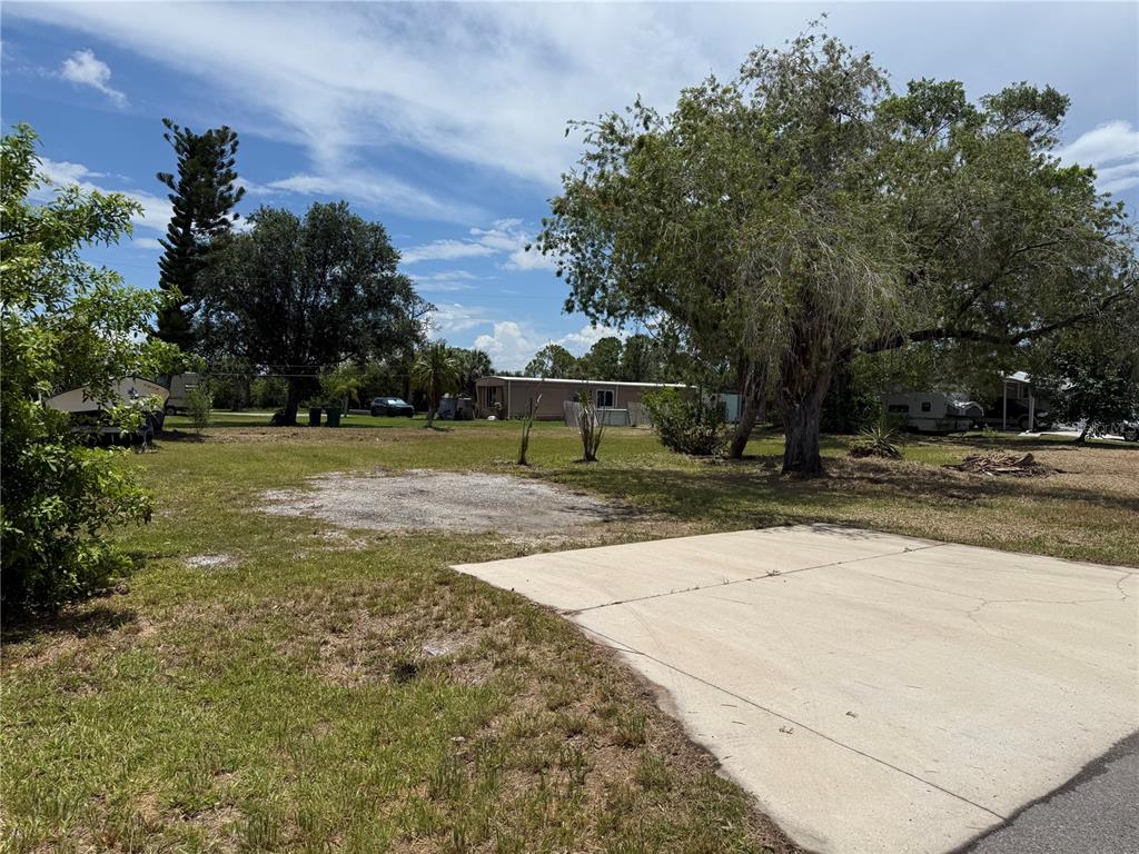 A concrete driveway leads to a grassy lot with trees and a mobile home — 3825 BRAVO ROAD, PORT CHARLOTTE, FL