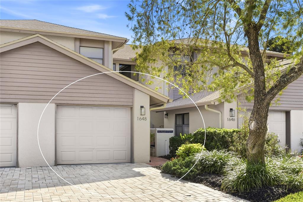The exterior of a two-story townhouse features a garage, a paved driveway, and landscaping — 1648 STARLING DRIVE UNIT 202, SARASOTA, FL