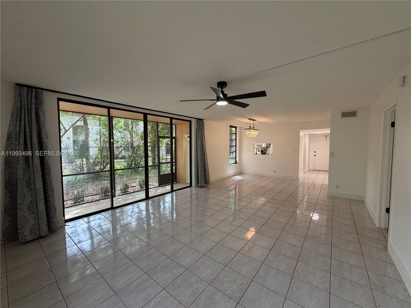 A spacious living room features light-colored tile flooring, a ceiling fan, and large sliding glass doors — 400 Commodore Dr # 101, Plantation FL 33325, PLANTATION, FL