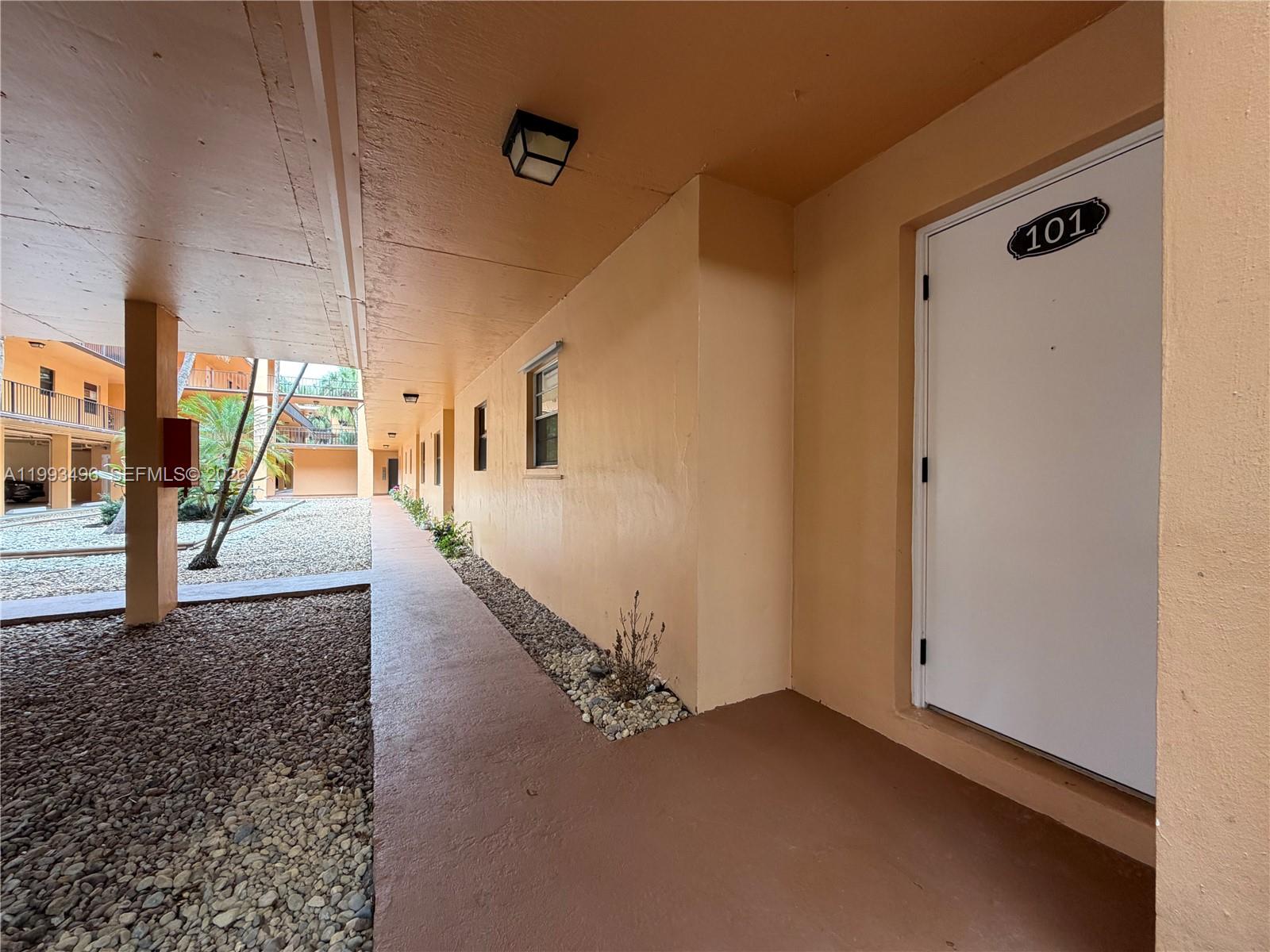 An exterior walkway leads past a white door marked 101 toward a courtyard — 400 Commodore Dr # 101, Plantation FL 33325, PLANTATION, FL