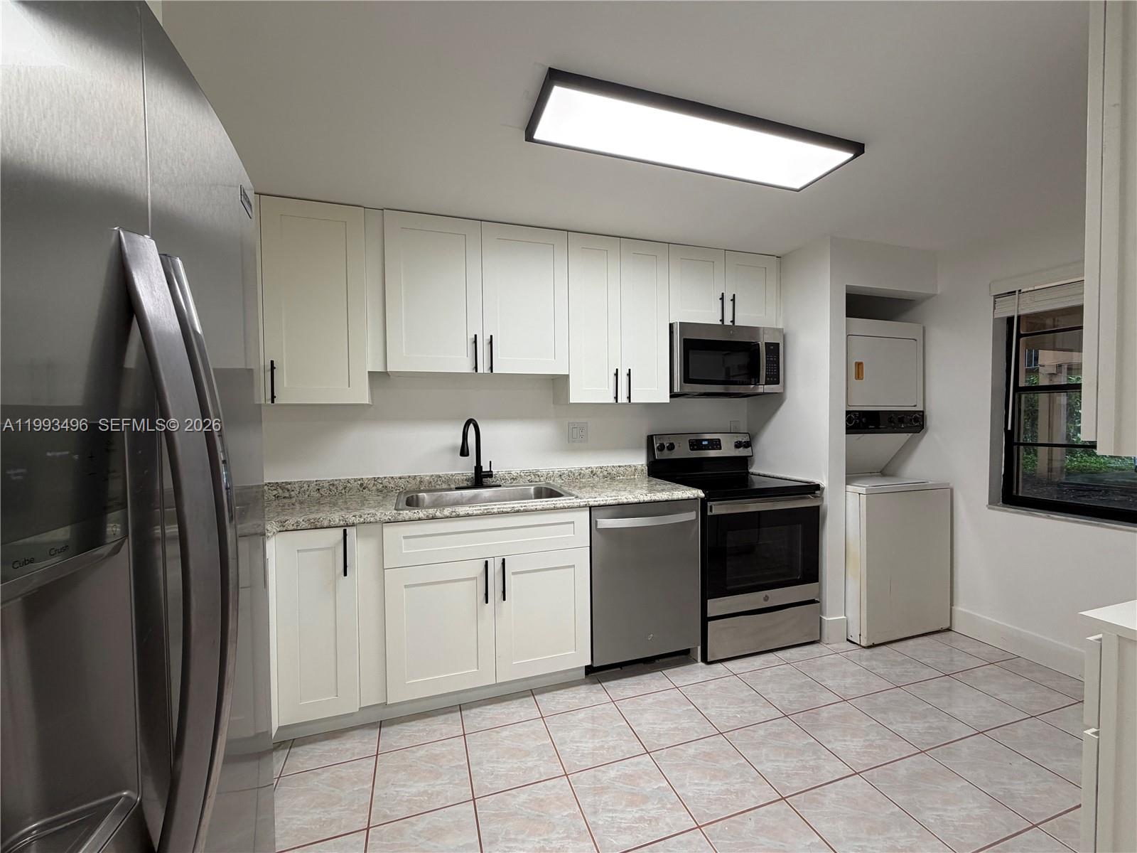 A kitchen features white cabinets, stainless steel appliances, granite countertops, and a stacked laundry unit — 400 Commodore Dr # 101, Plantation FL 33325, PLANTATION, FL