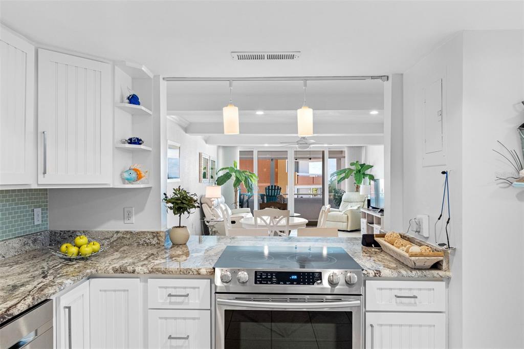 A kitchen with white cabinets and granite countertops looks out toward a bright living area — 17920 GULF BOULEVARD UNIT 302, REDINGTON SHORES, FL