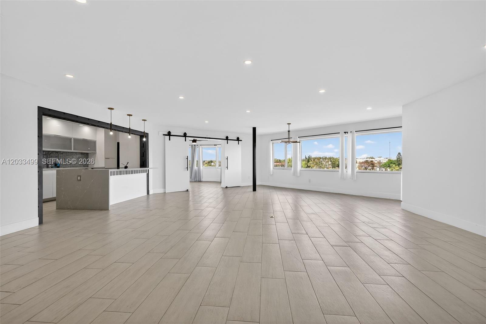 An open-concept living area features light wood-look tile flooring, white walls, and a kitchen island — 877 NE 195th St # 422, Miami FL 33179, MIAMI, FL