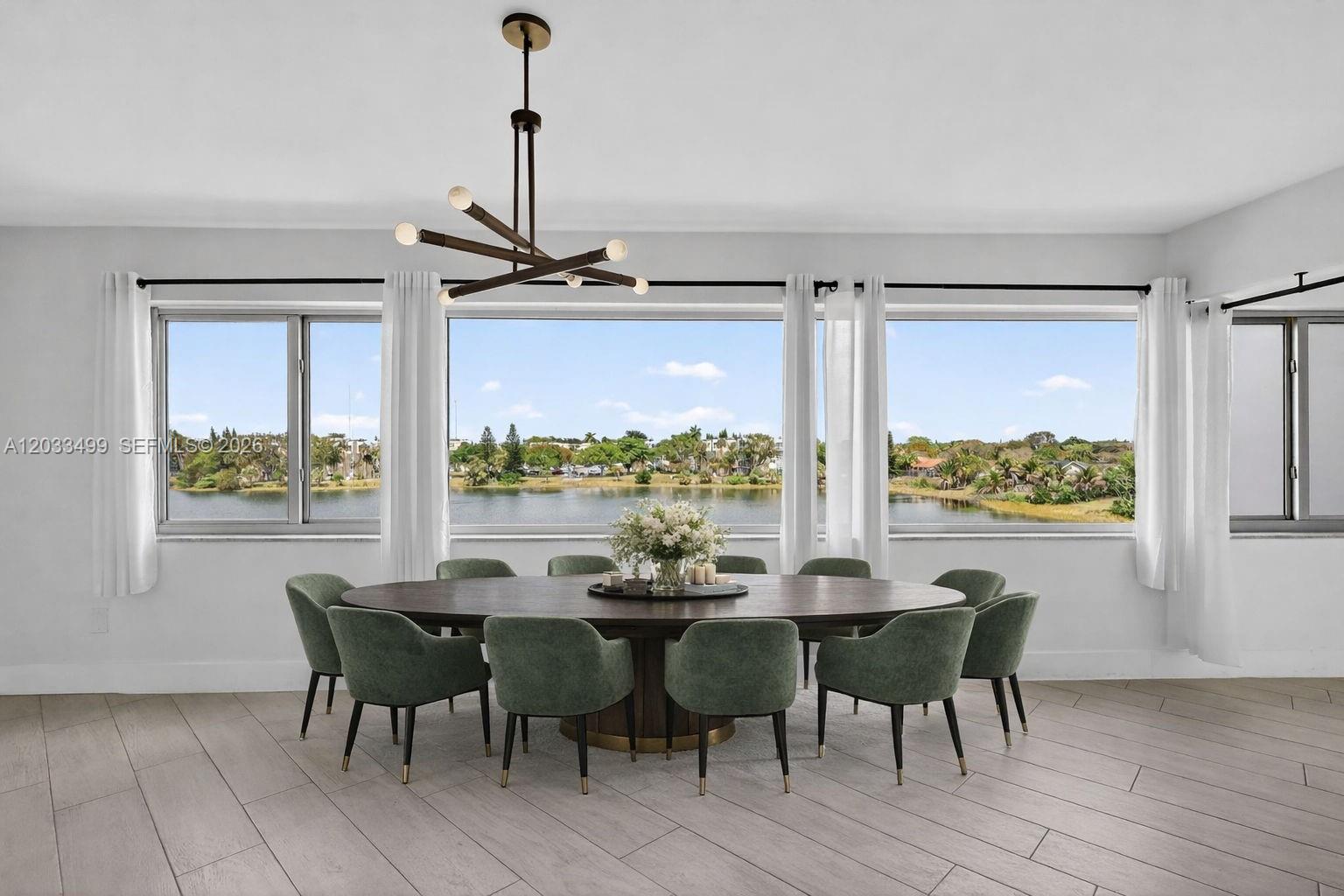 A dining room features a large oval table, green chairs, and windows overlooking a lake — 877 NE 195th St # 422, Miami FL 33179, MIAMI, FL