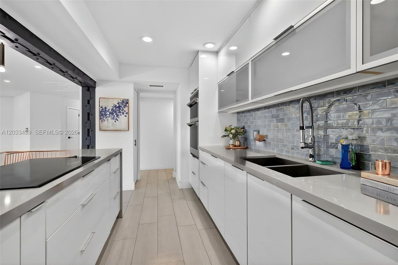 A modern galley kitchen features white glossy cabinets, gray countertops, and a blue tiled backsplash — 877 NE 195th St # 422, Miami FL 33179, MIAMI, FL