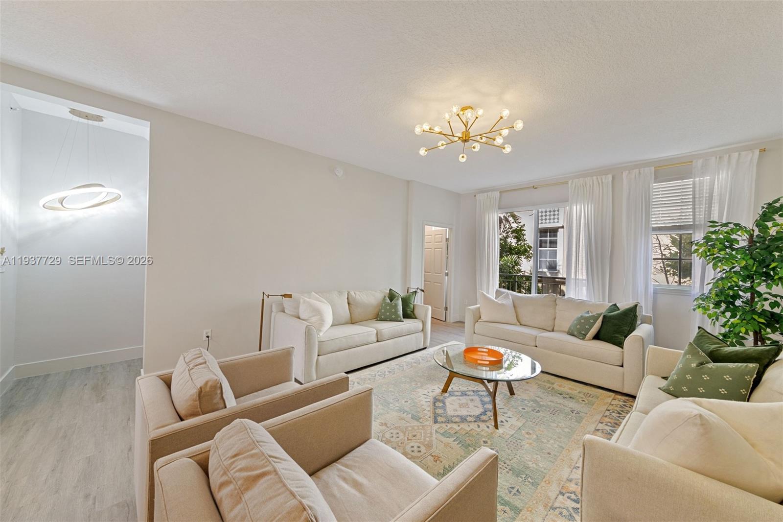 A bright living room features light-colored sofas, a glass coffee table, and a modern chandelier — 2067 S Ocean Dr, Hallandale Beach FL 33009, HALLANDALE BEACH, FL