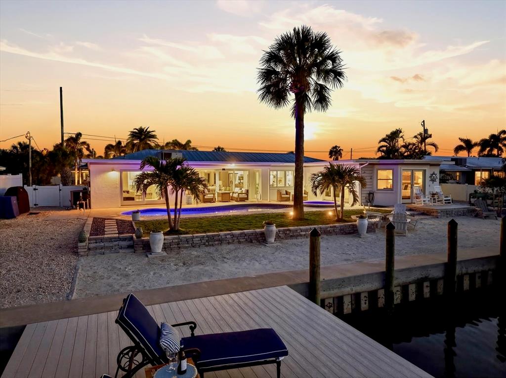A waterfront house with a pool, palm trees, and a wooden dock at sunset — 617 DUNDEE LANE, HOLMES BEACH, FL