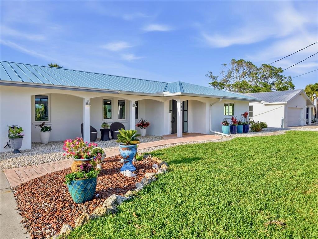 A single-story house with a blue metal roof, white exterior, and a landscaped front yard — 617 DUNDEE LANE, HOLMES BEACH, FL