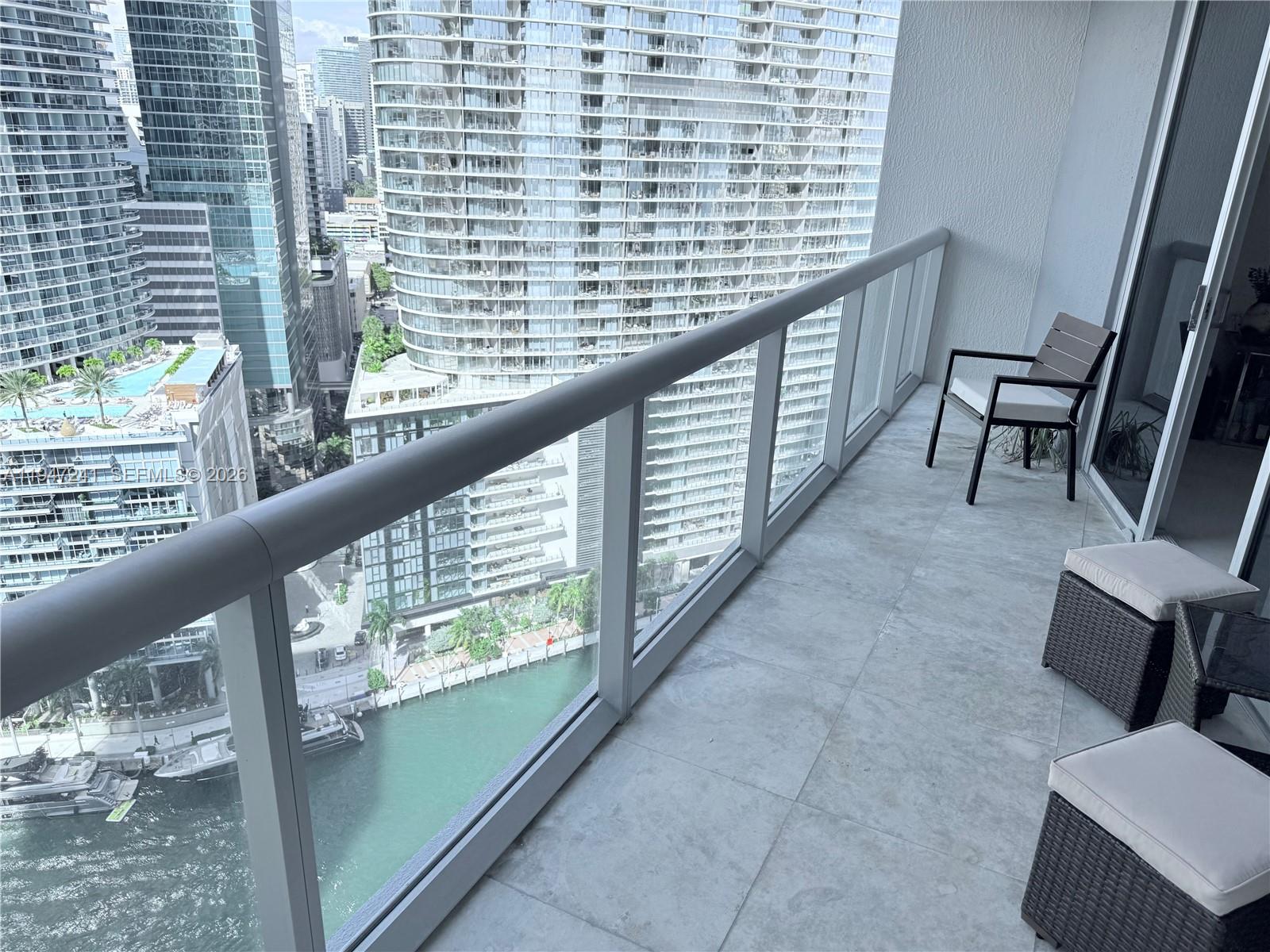 A balcony with tiled flooring overlooks a city waterway and surrounding high-rise buildings — 465 Brickell Ave # 2906, Miami FL 33131, MIAMI, FL