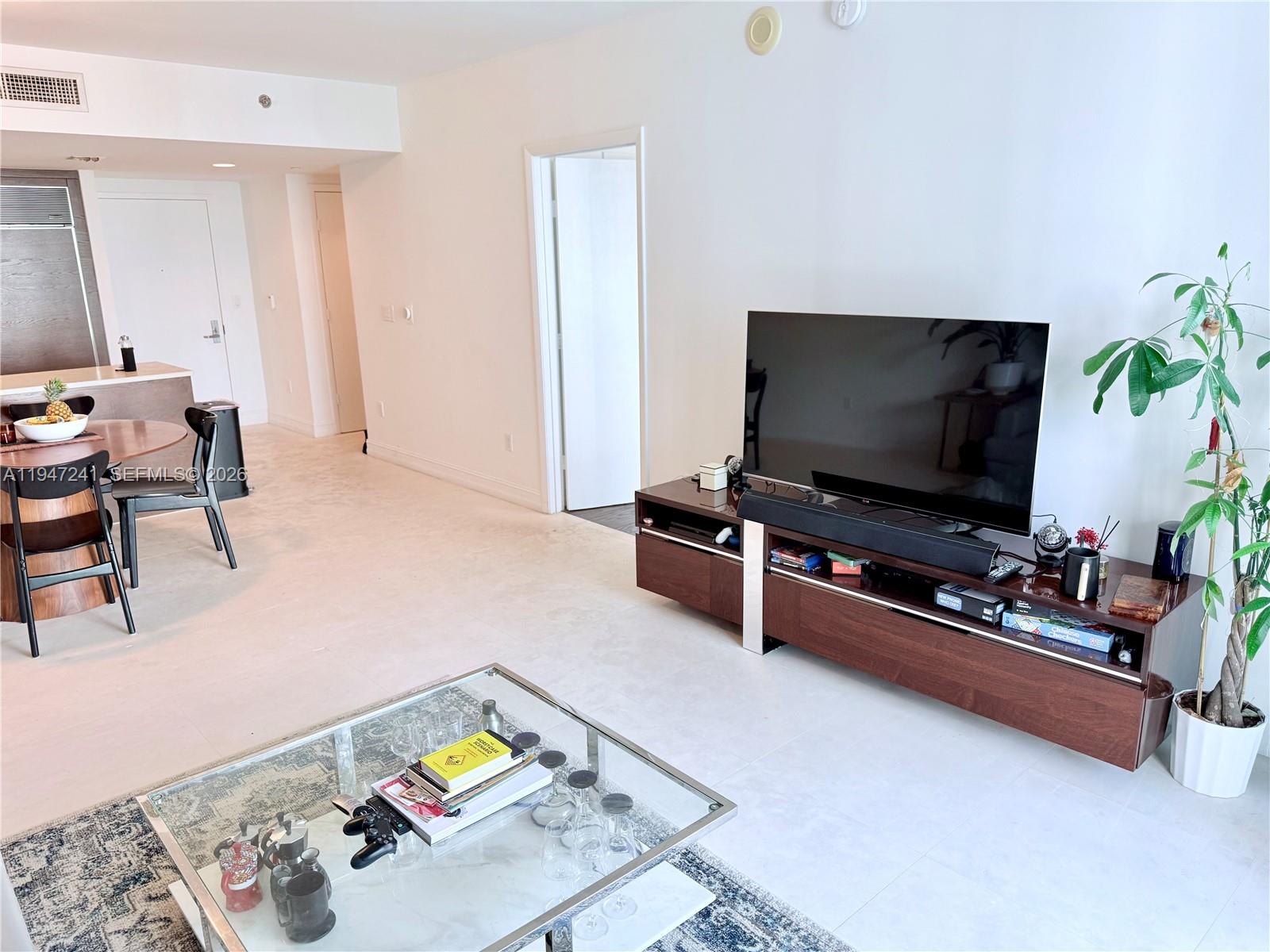 A living room features a television on a wooden console, a glass coffee table, and a dining area — 465 Brickell Ave # 2906, Miami FL 33131, MIAMI, FL