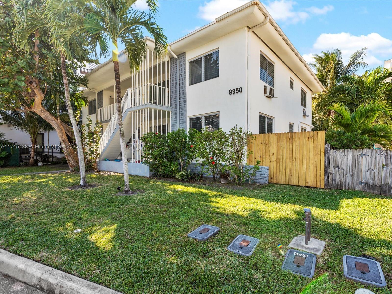 A two-story apartment building features white stucco walls, exterior stairs, and a wooden fence — 9950 E Bay Harbor Dr, Bay Harbor Islands FL 33154, BAY HARBOR ISLANDS, FL