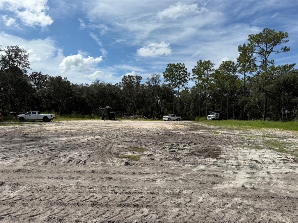 A large, cleared dirt lot features several parked trucks and a dense treeline background — TBD SW 146TH LANE ROAD, DUNNELLON, FL