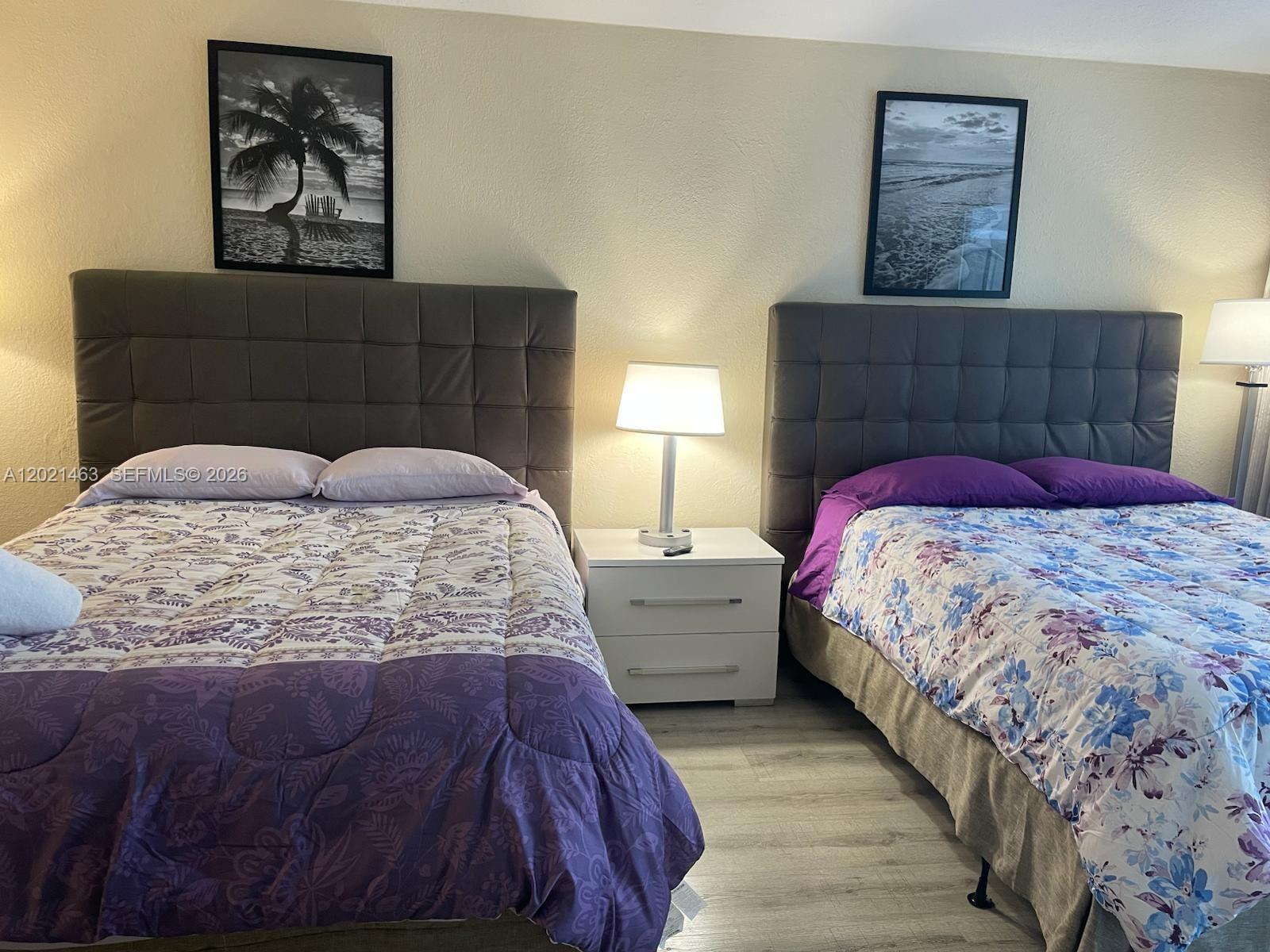 A bedroom features two beds with tufted headboards, a nightstand, and framed wall art — SUNNY ISLES BEACH, FL