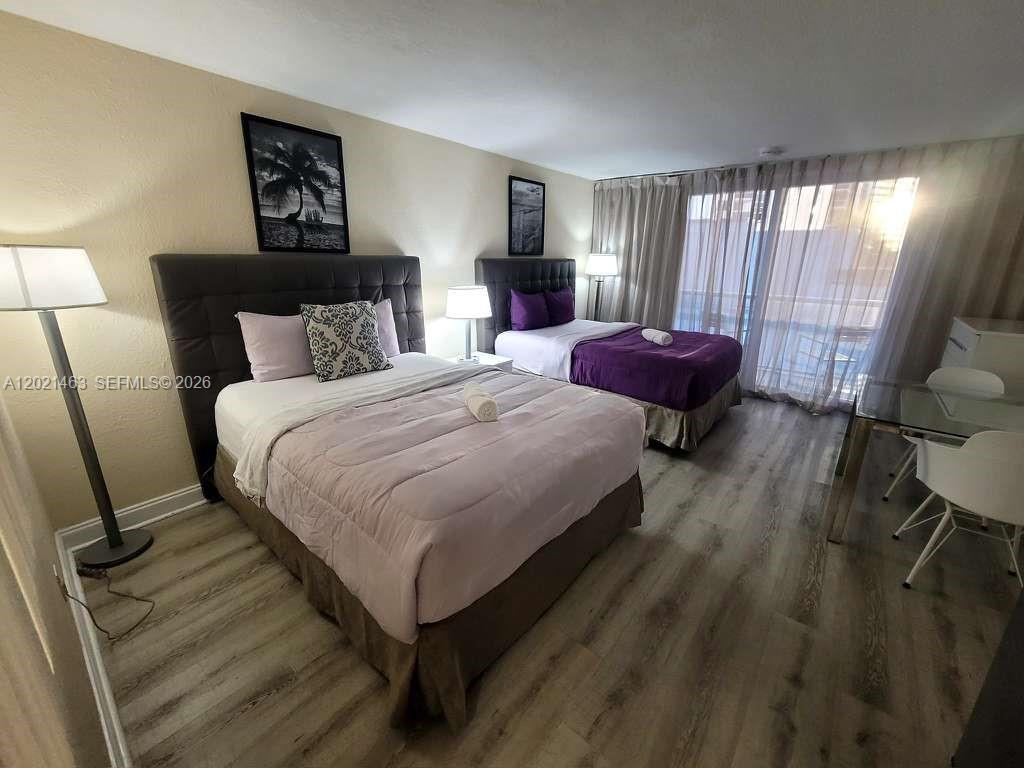 A bedroom features two beds with dark headboards, light wood-look flooring, and a glass balcony door — SUNNY ISLES BEACH, FL