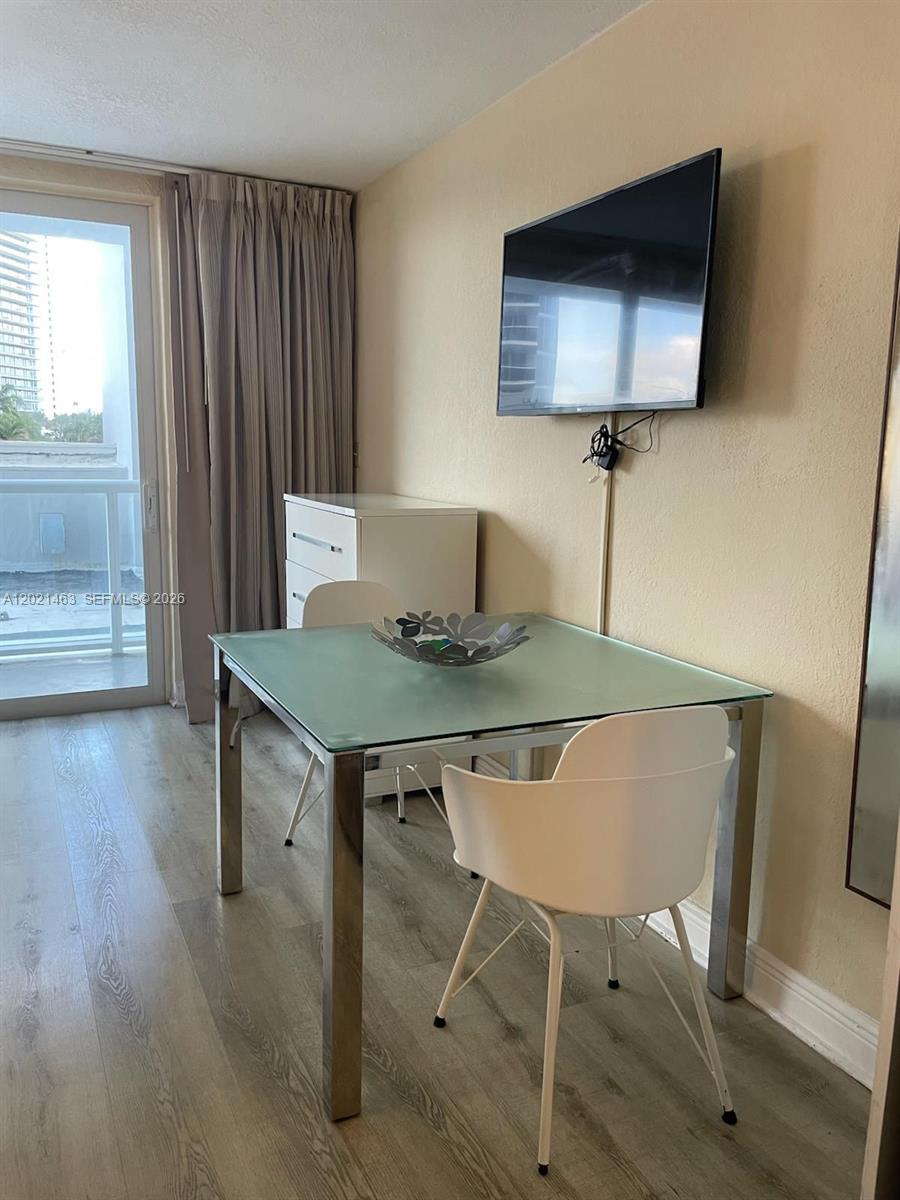 A dining area features a glass-topped table, white chairs, and a wall-mounted television — SUNNY ISLES BEACH, FL
