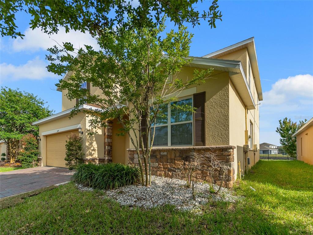 A two-story house with a tan stucco exterior, stone accents, and a paved driveway — 624 SARDINIA CIRCLE, DAVENPORT, FL