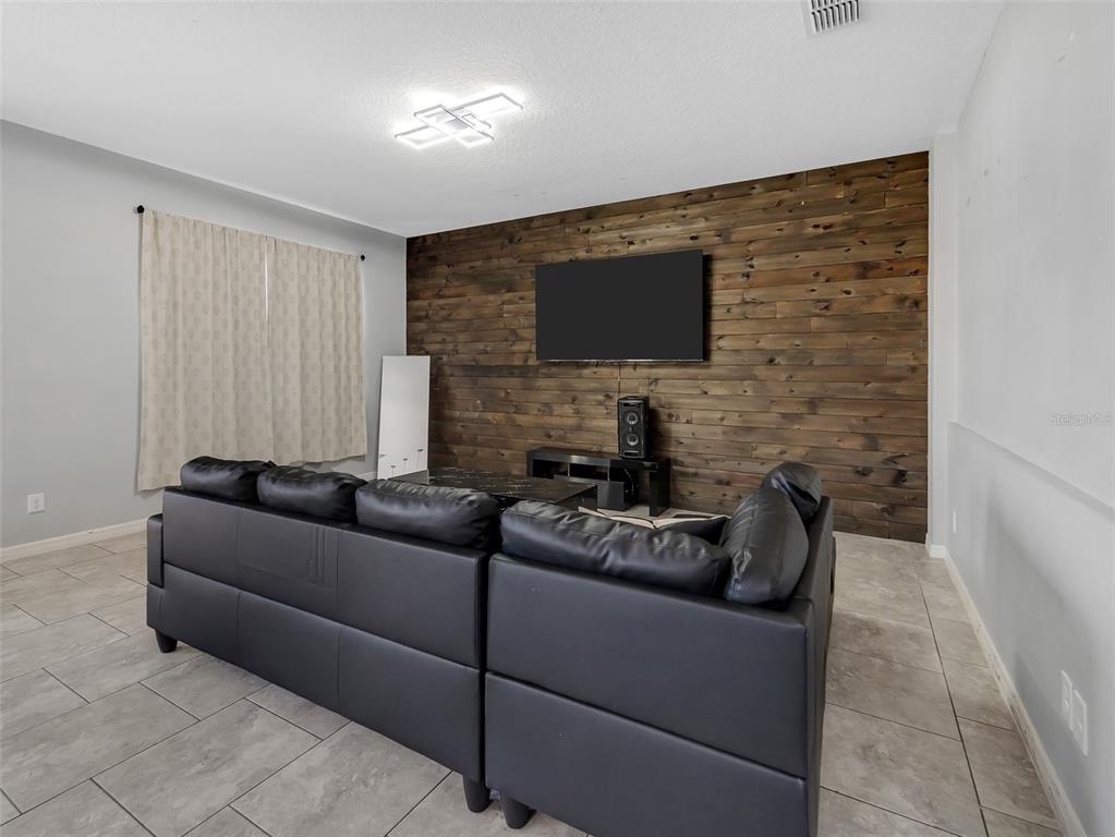 A living room features a dark wood accent wall, a black sectional sofa, and tile flooring — 624 SARDINIA CIRCLE, DAVENPORT, FL