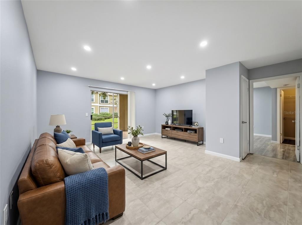 A living room features light gray walls, tile flooring, a leather sofa, and a television console — 9481 HIGHLAND OAK DRIVE UNIT 1502, TAMPA, FL