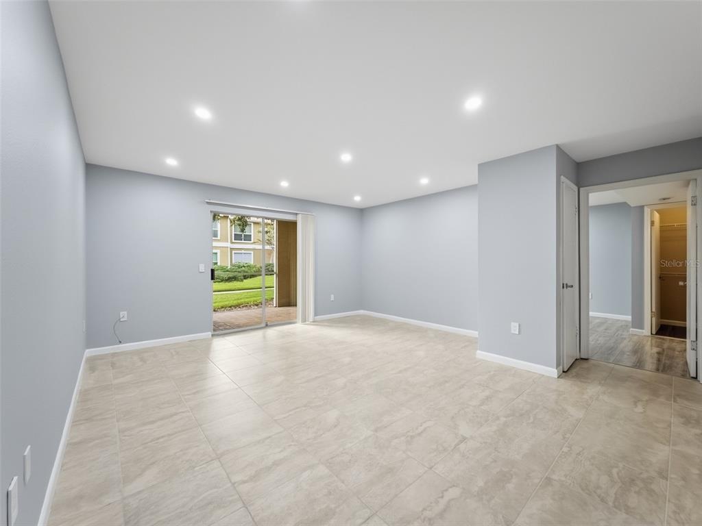 An empty living room features light gray walls, large beige floor tiles, and a sliding door — 9481 HIGHLAND OAK DRIVE UNIT 1502, TAMPA, FL