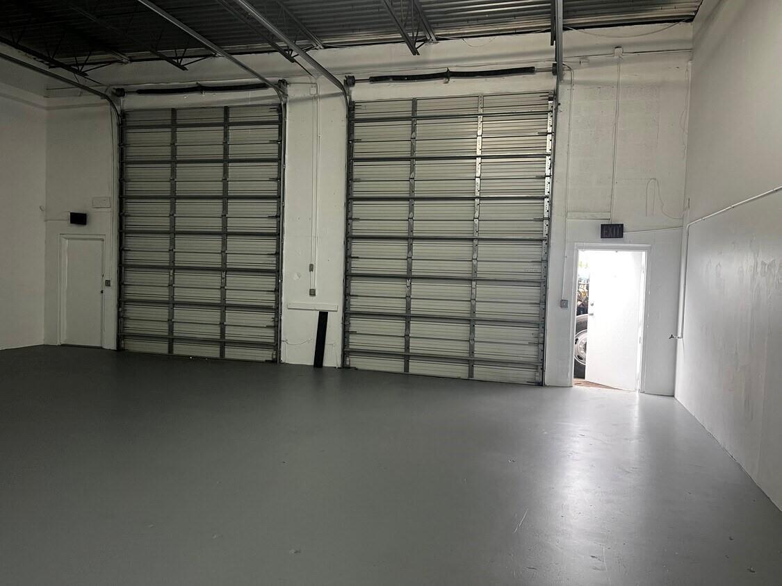 An empty warehouse space with gray floors, two large roll-up doors, and two exit doors — 7641 Hooper Road, West Palm Beach FL 33411, WEST PALM BEACH, FL