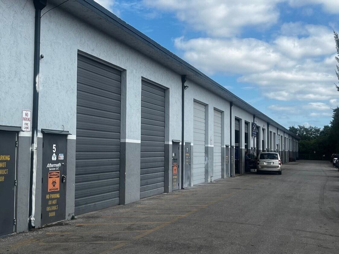 An exterior view of a row of industrial warehouse units with gray roll-up doors — 7641 Hooper Road, West Palm Beach FL 33411, WEST PALM BEACH, FL