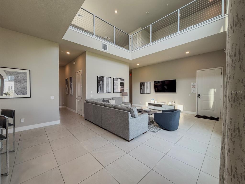 A bright living room features a high ceiling, tile floors, and a large gray sectional — 7770 SANDY RIDGE DRIVE UNIT 231, REUNION, FL