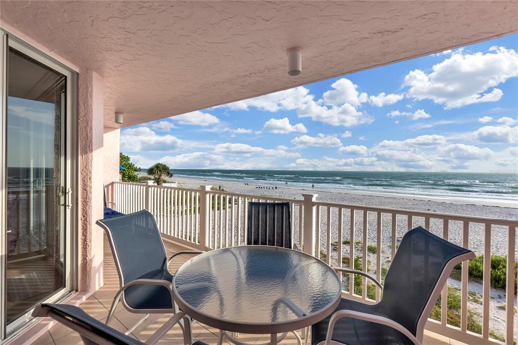 A balcony with a glass table and chairs overlooks a sandy beach and the ocean — 2600 GULF DRIVE N UNIT 12, BRADENTON BEACH, FL