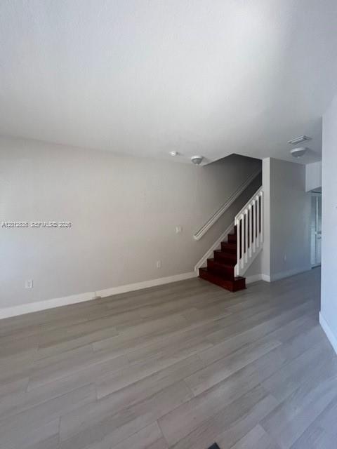An empty room with light wood-look flooring and a staircase with dark wood steps — 2573 SW 121st Ter # 2003, Miramar FL 33025, MIRAMAR, FL