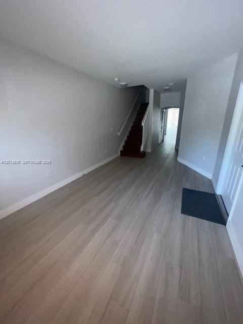 An empty room with light wood-look flooring, white walls, and a staircase leading upstairs — 2573 SW 121st Ter # 2003, Miramar FL 33025, MIRAMAR, FL
