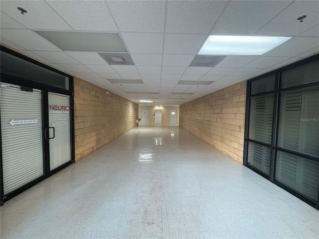 A long, narrow commercial hallway features tan block walls, a drop ceiling, and light flooring — 13250 N 56TH STREET UNIT 103, TEMPLE TERRACE, FL