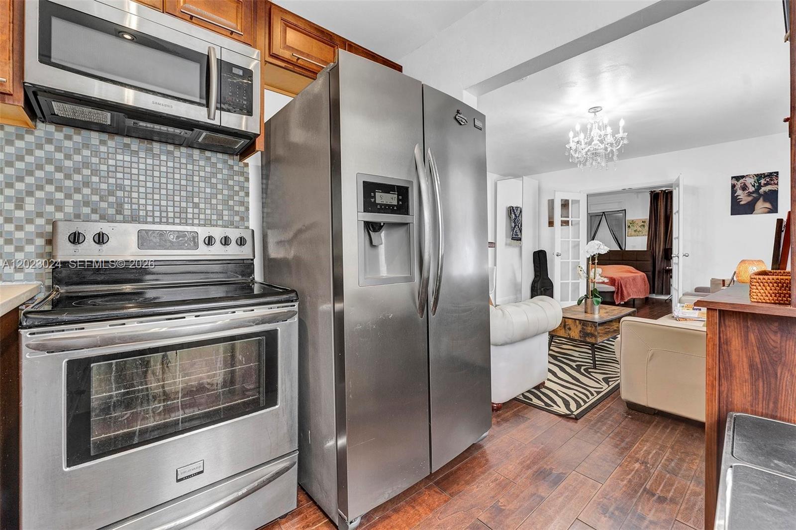 A kitchen with stainless steel appliances and a mosaic backsplash opens into a living area — 1150 Euclid Ave # 101, Miami Beach FL 33139, MIAMI BEACH, FL