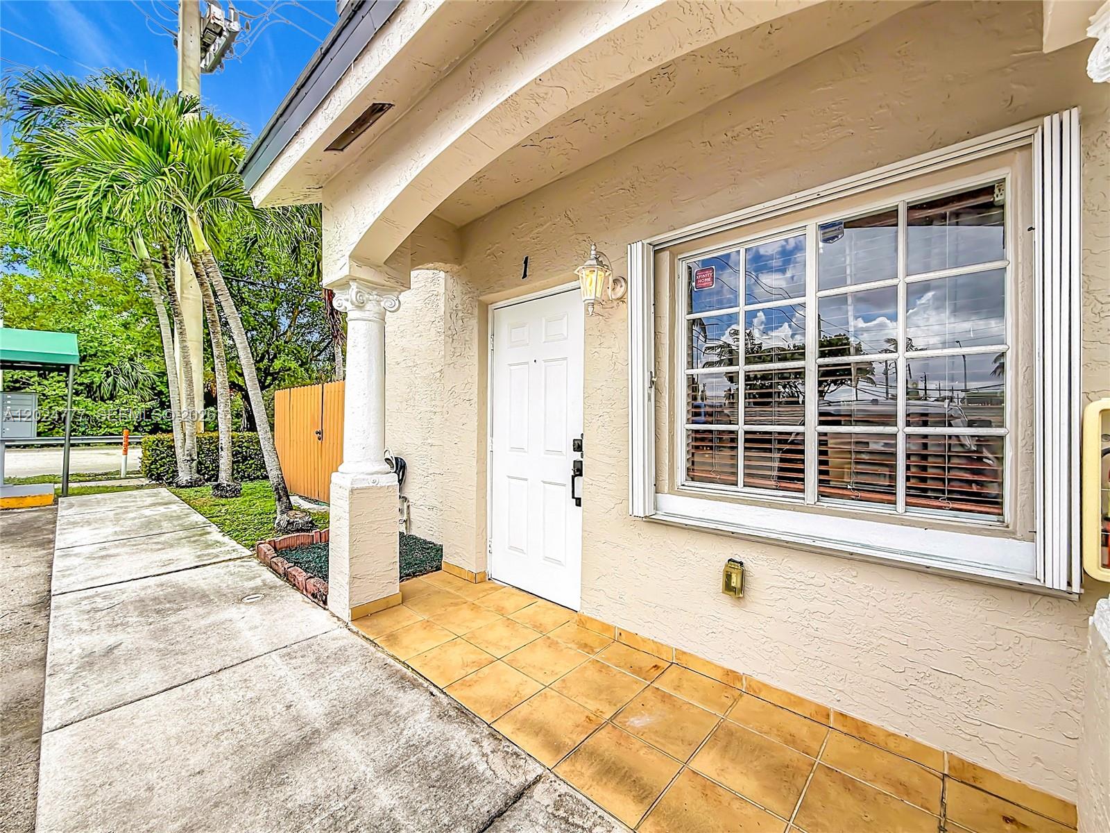 The exterior of a house features a white front door, tiled porch, and large window — 7699 W 36th Ave # 1, Hialeah FL 33018, HIALEAH, FL